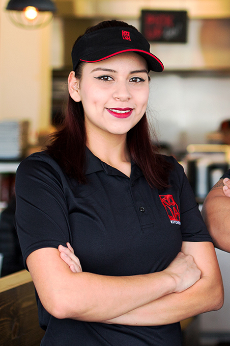 Image contains: Latina Female with a big smile and wearing KoJa Kitchen shirt with interior of a restaurant in background